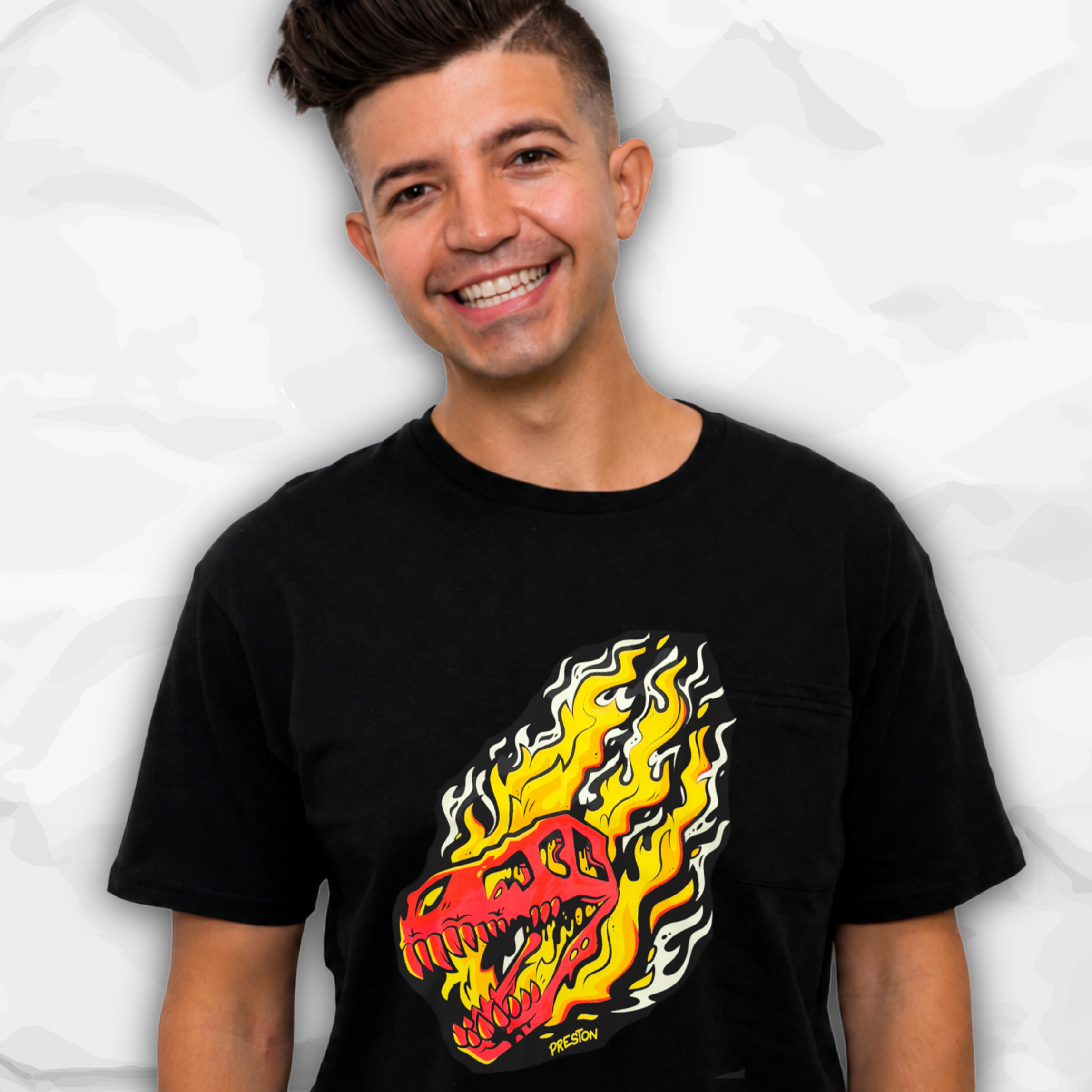 Preston Playz wearing a black short-sleeve t-shirt with a graphic of a red and yellow flaming dinosaur head on the front, set against a light gray crumpled paper background.
