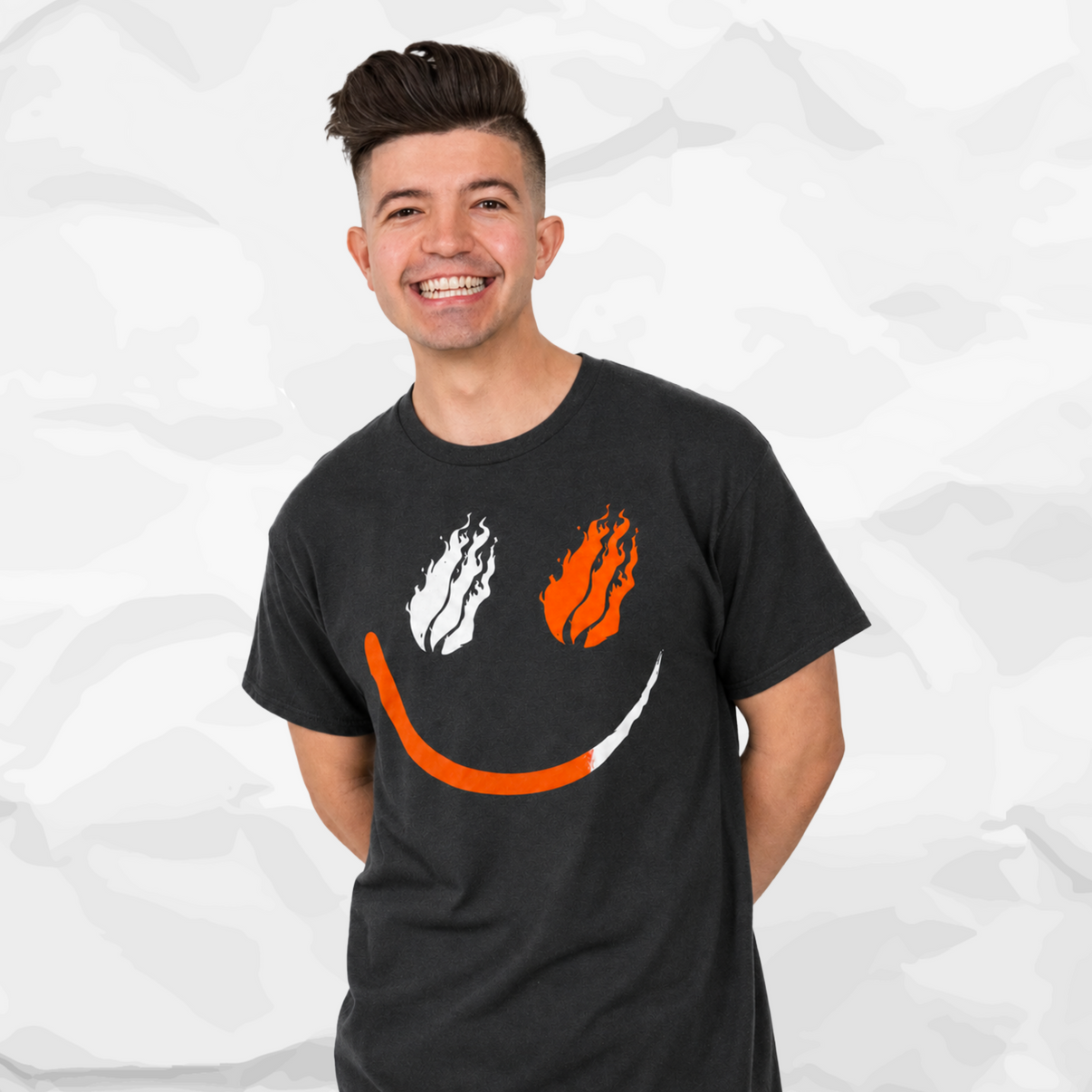 Preston Stylez wearing a drak gray t-shirt with a graphic of white and orange flames forming a smiley face, set against a light gray crumpled paper background.